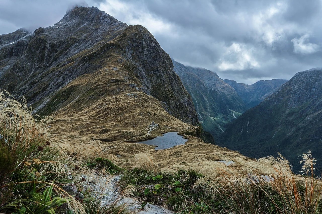 Rocky trail leading to a small tarn beneath steep mountains on the Milford Track, New Zealand