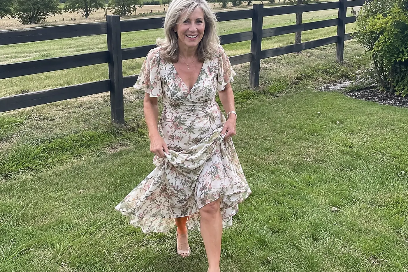 Older woman walking on grass in a flowing midi dress outside a wedding venue.