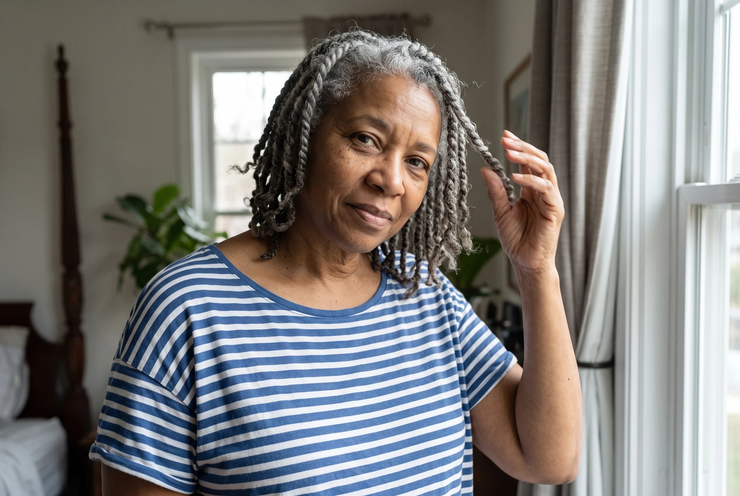 A woman in her sixties wearing a blue striped cotton tee touches her grey hair.