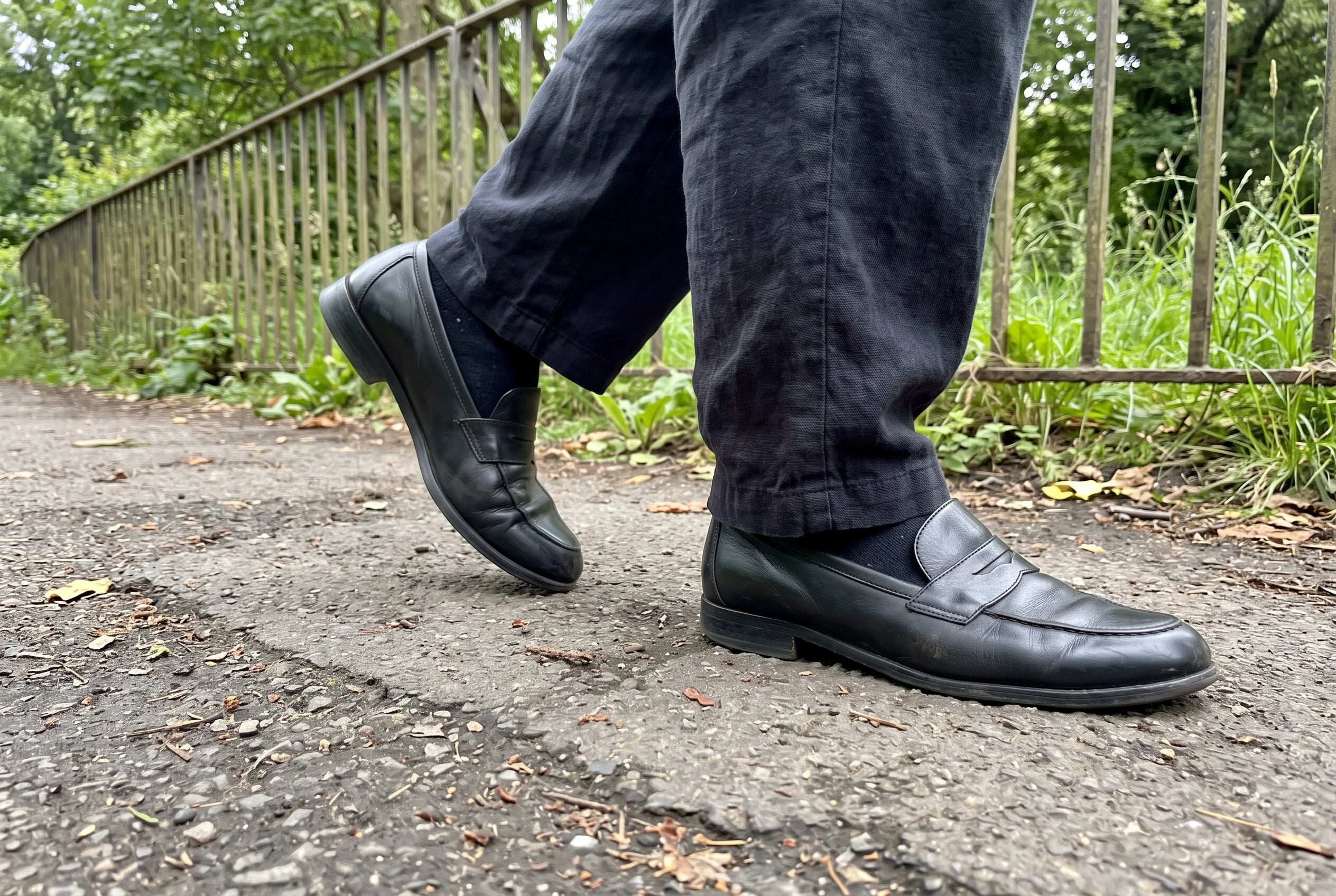 A woman in dark trousers and black leather loafers walks along a park path.