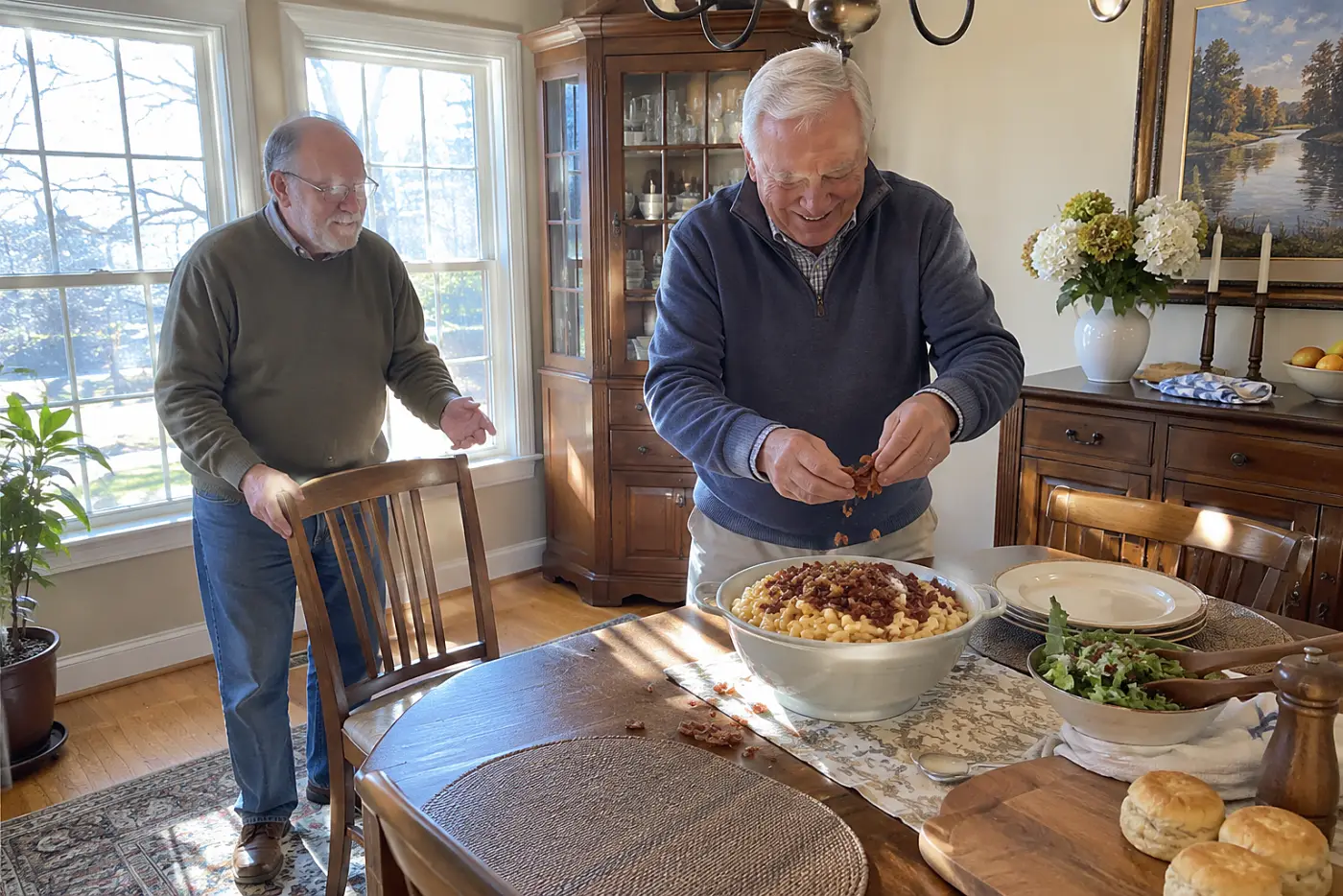 A man crumbles cooked bacon over macaroni in a dining room.
