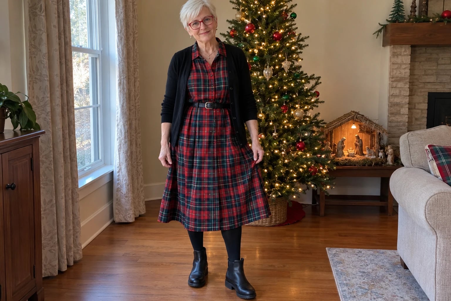 A woman in her sixties wears a red tartan shirtdress with a black cardigan, opaque tights and ankle boots by a lit Christmas tree.