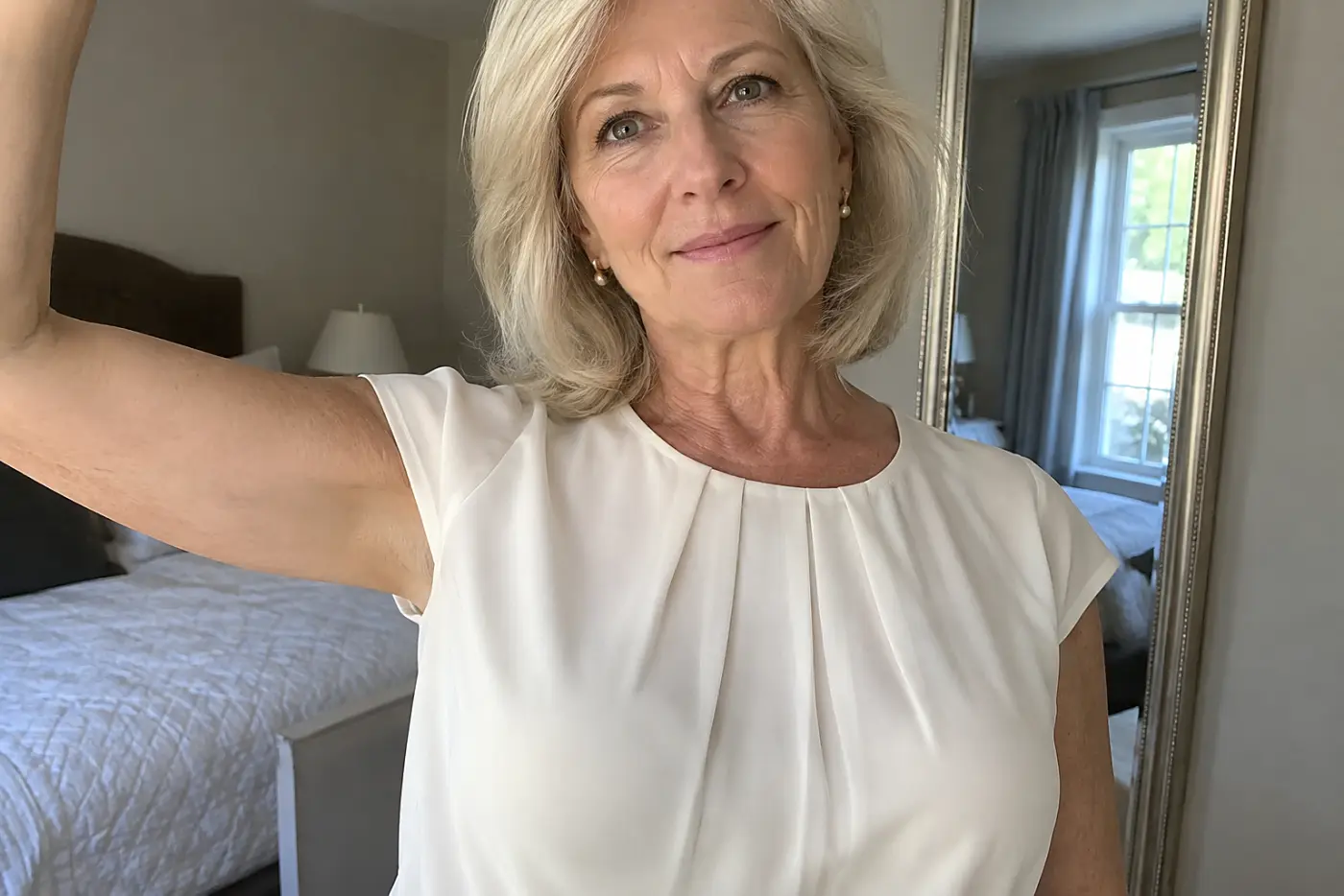 A woman in her sixties wears a white cap-sleeve blouse while raising an arm.