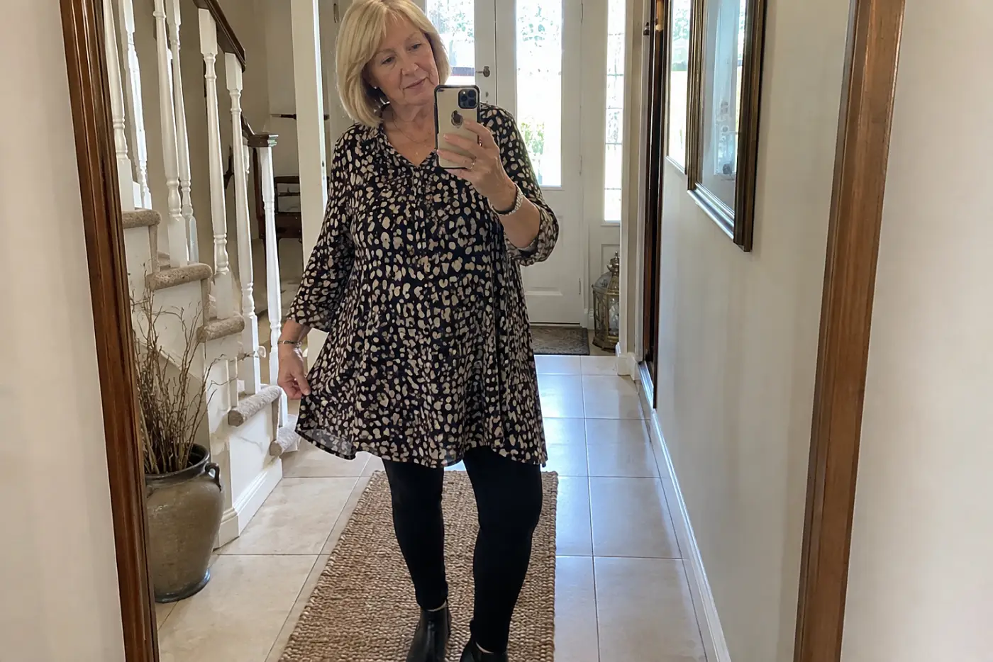 A woman in her sixties wears a patterned tunic over black leggings.