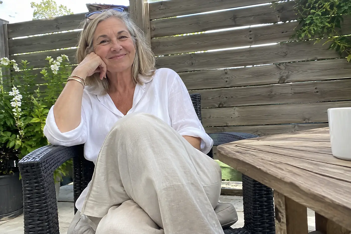 Wrinkled linen pants are centered on a woman over 60 sitting at an outdoor café table.