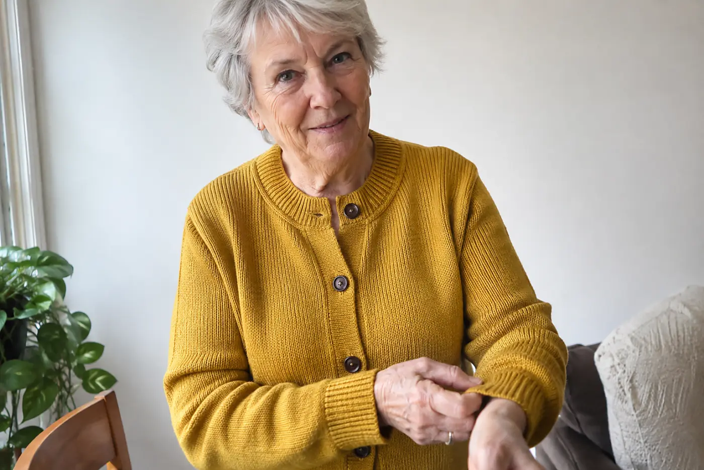 A woman in her seventies wearing a mustard yellow cardigan adjusts her sleeve.