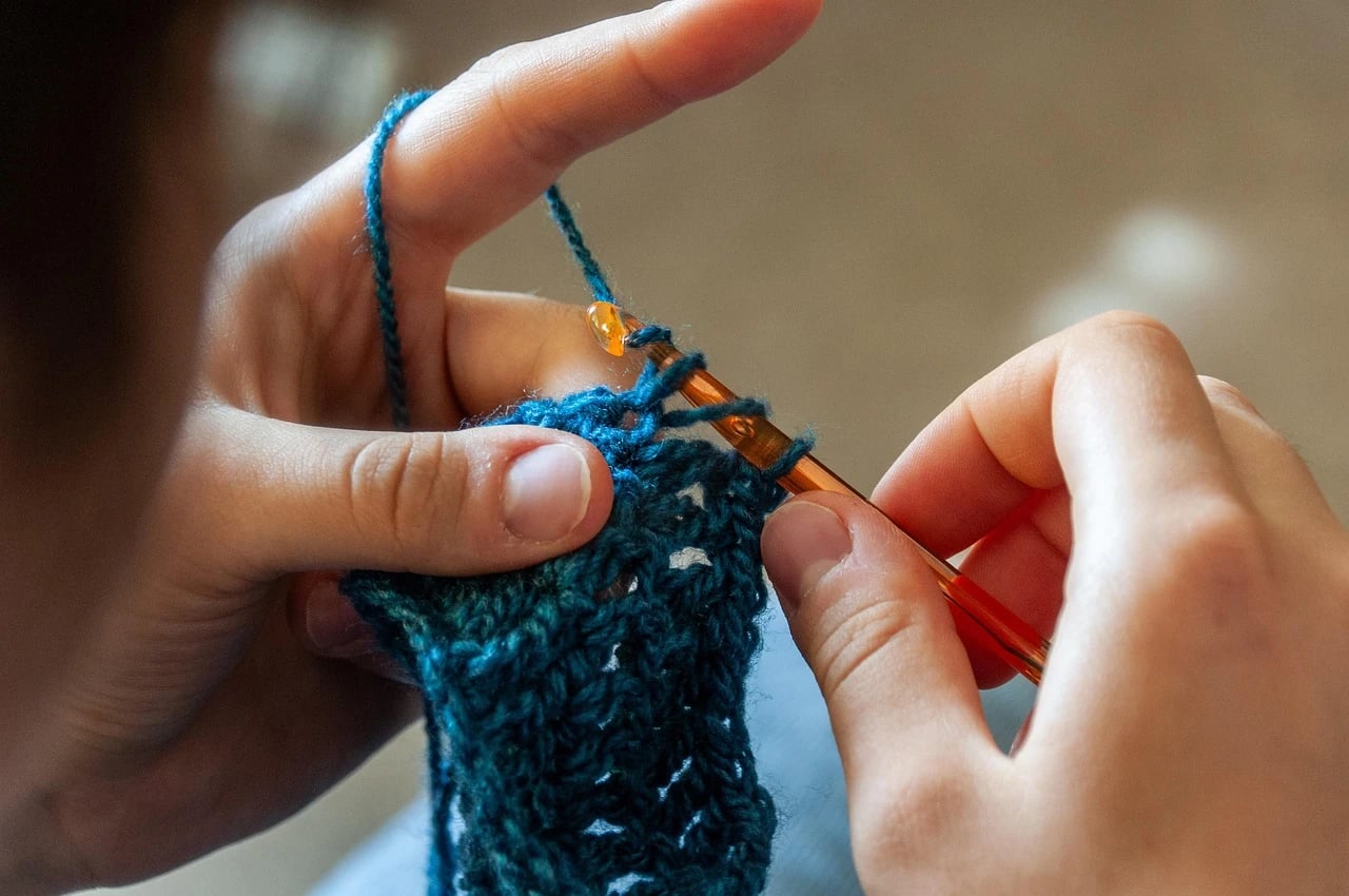 Close-up of hands crocheting teal yarn with an orange crochet hook