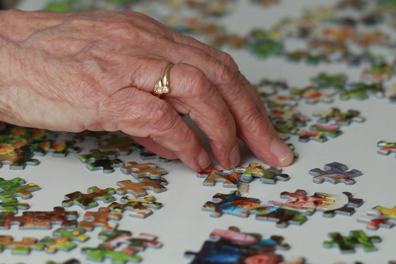 Close-up of an older woman's hand with a gold ring resting among scattered jigsaw puzzle pieces