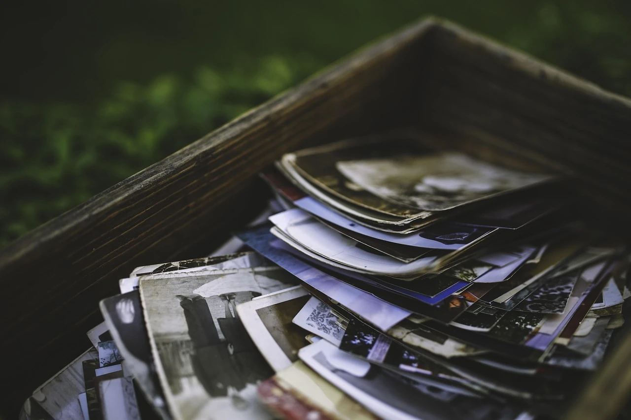 Wooden box overflowing with a pile of old printed photographs, set against green grass