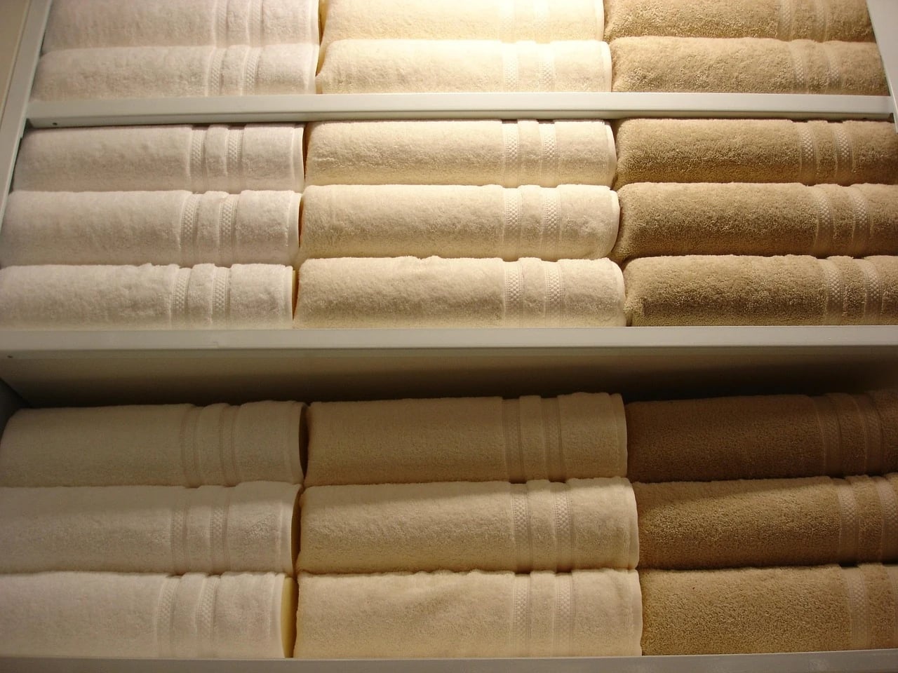 Rows of folded cream, beige and tan towels stacked neatly on white shelves