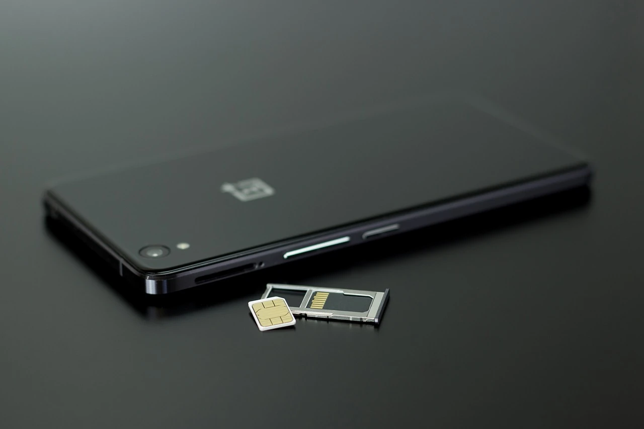 Black smartphone lying on a dark glossy surface with a SIM card and ejected SIM tray beside it