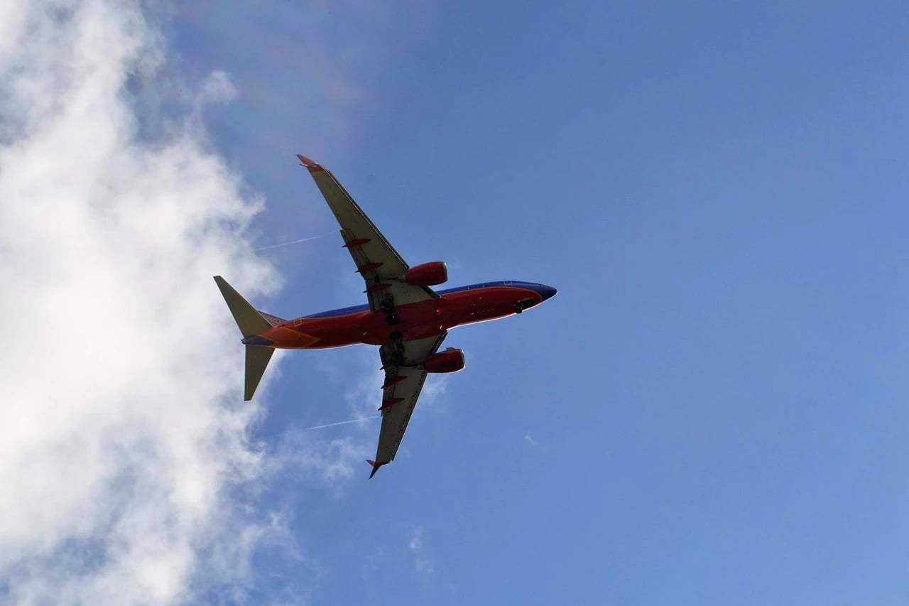 Red, blue and orange Southwest Airlines jet flying overhead against a blue sky with white clouds