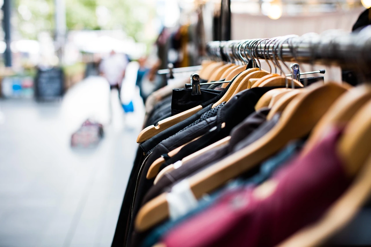 Close-up of jackets and shirts on wooden hangers along a metal clothing rack, with a blurred street behind