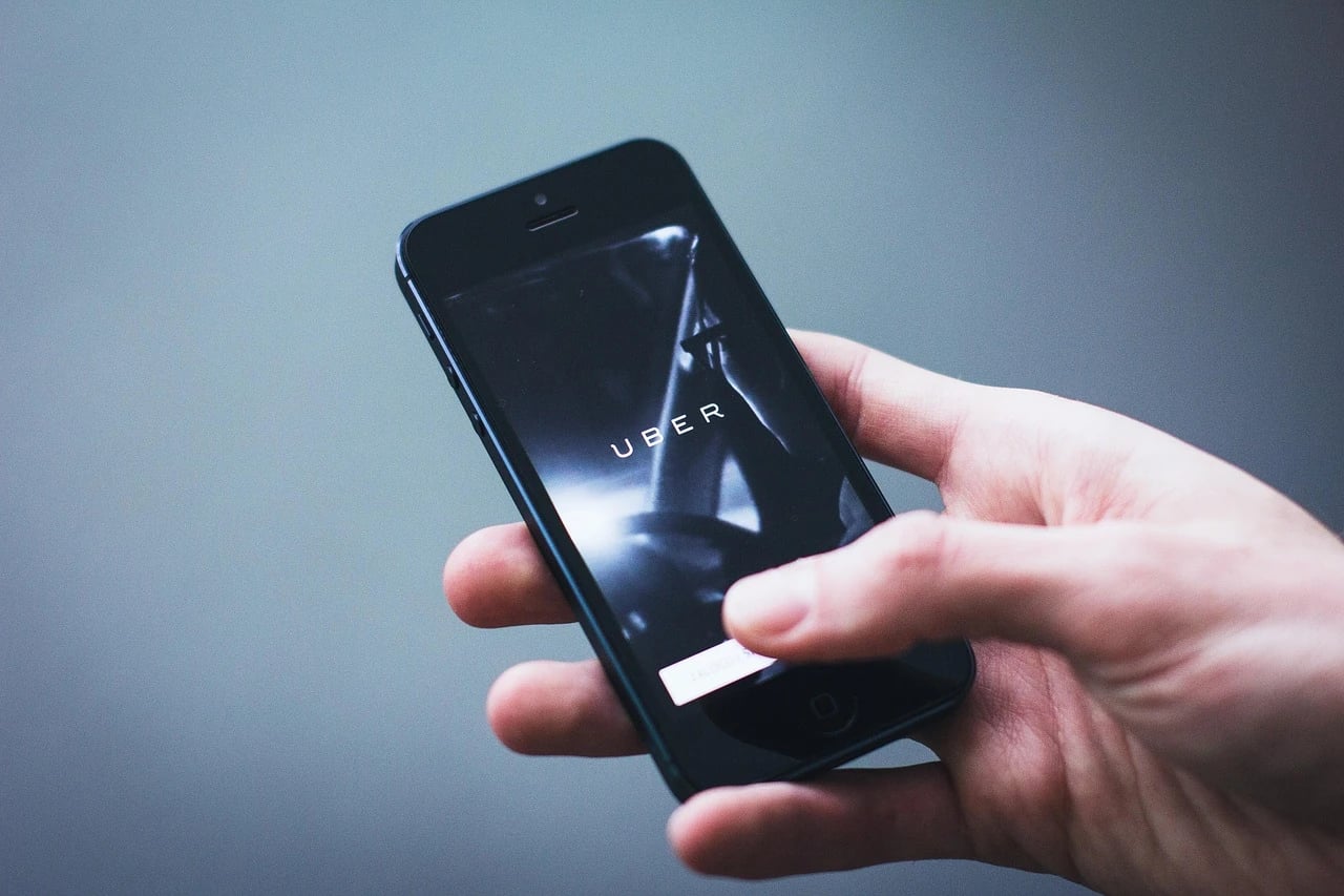 Hand holding a black smartphone showing the Uber app launch screen against a gray background