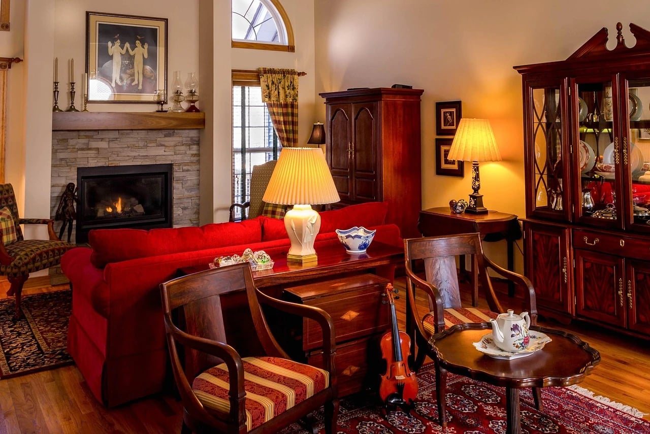 Warmly lit living room with antique china cabinet, wooden chairs, red sofa, violin and tea set on table