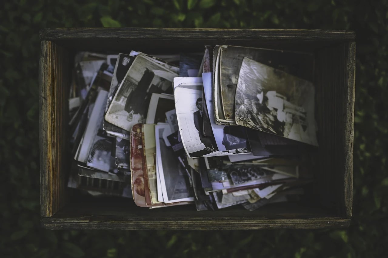 Overhead view of a weathered wooden box filled with old vintage family photographs resting on dark grass