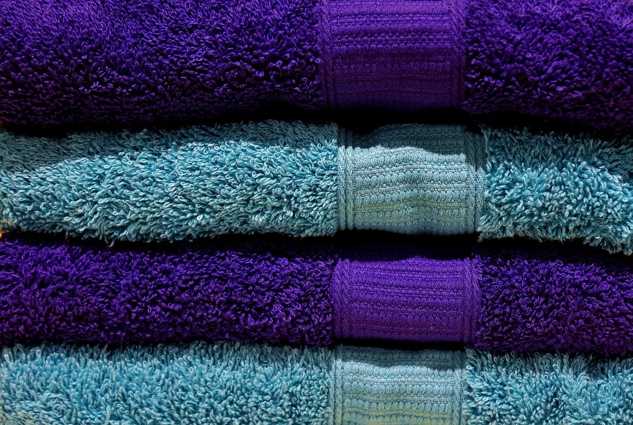 Close-up of neatly stacked folded purple and teal terry towels in alternating layers