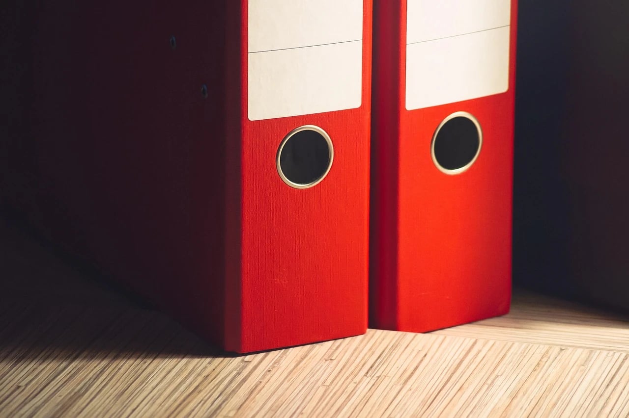 Two red office binders with blank spine labels standing side by side on a wooden surface