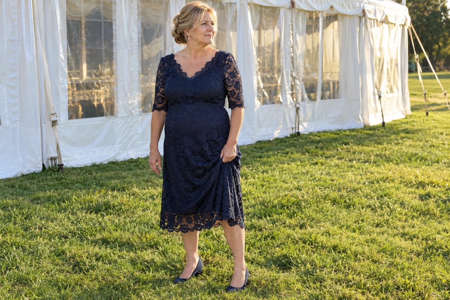 A woman in her late fifties stands on the lawn in a navy lace knee-length dress and navy heels.