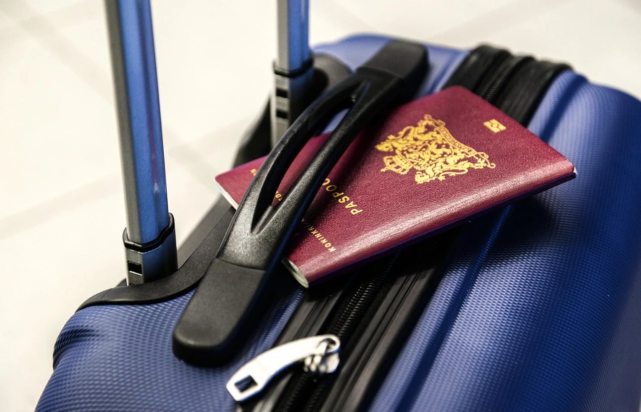 Burgundy Dutch passport lying on top of a blue hard-shell suitcase beside its handle