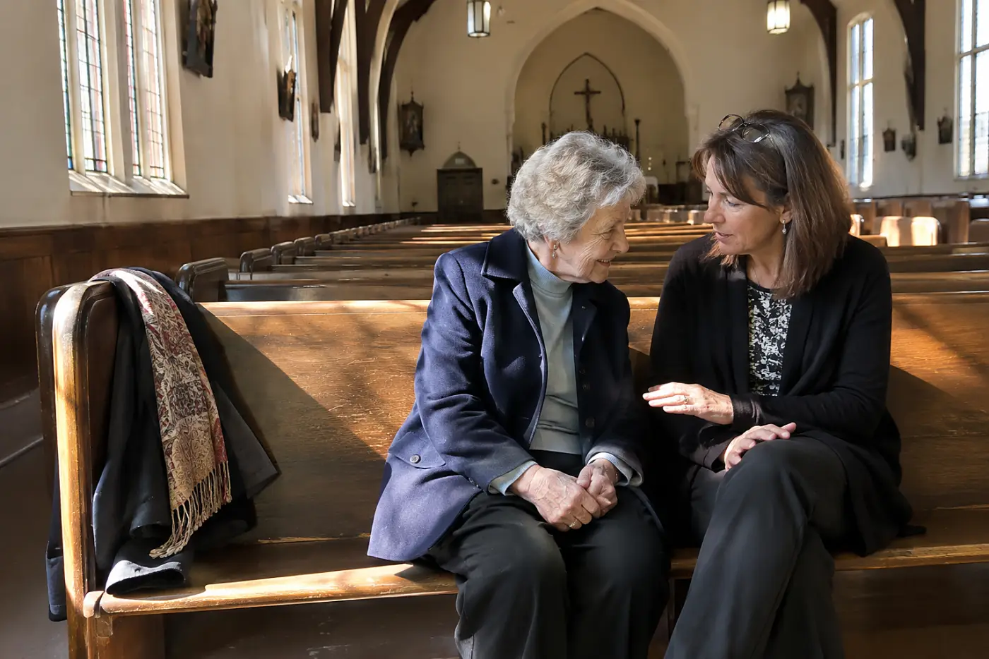 A woman in her 70s sitting with her daughter in an empty church pew.