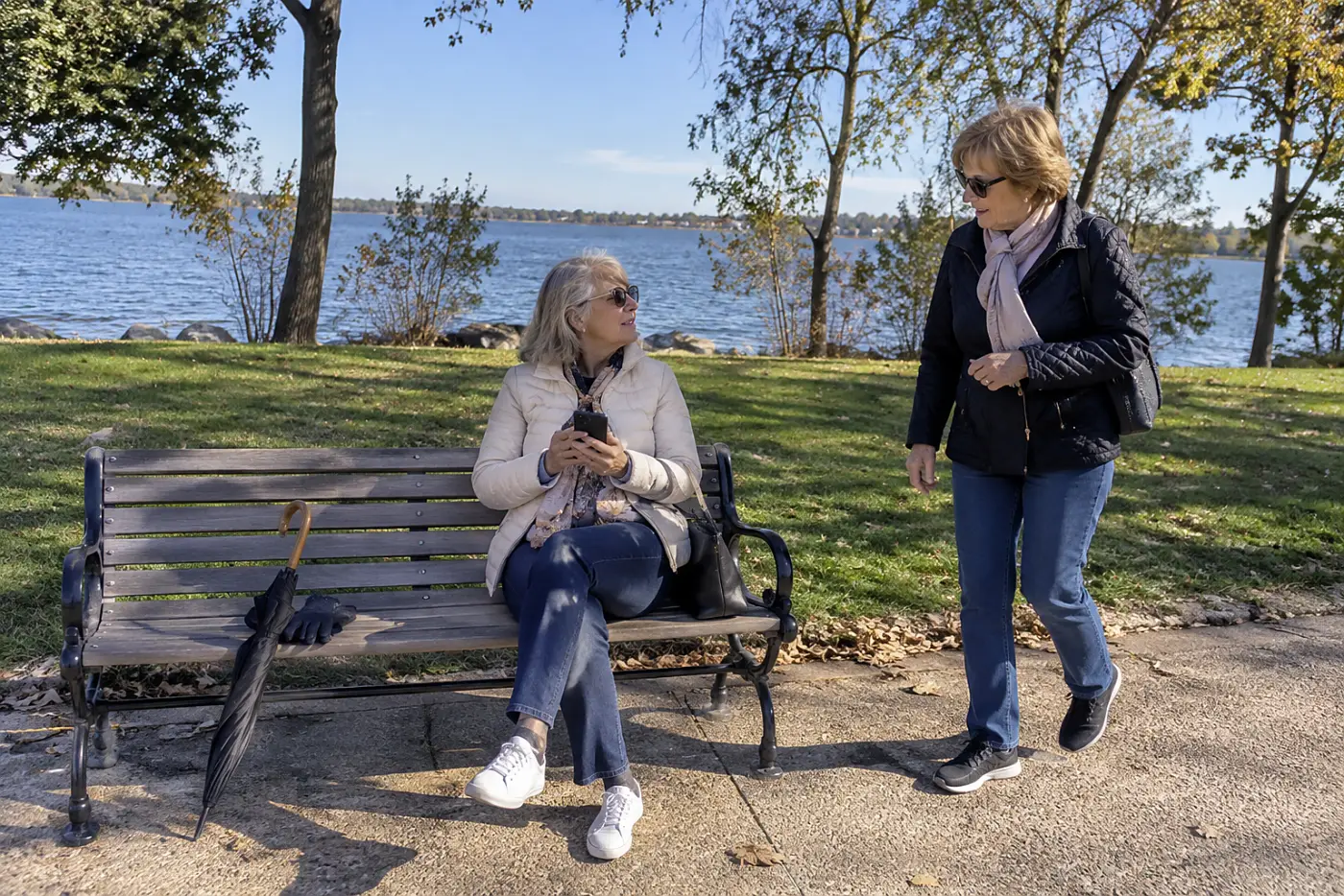 A woman in her 60s looking at her phone while seated on a park bench, with the screen turned away.