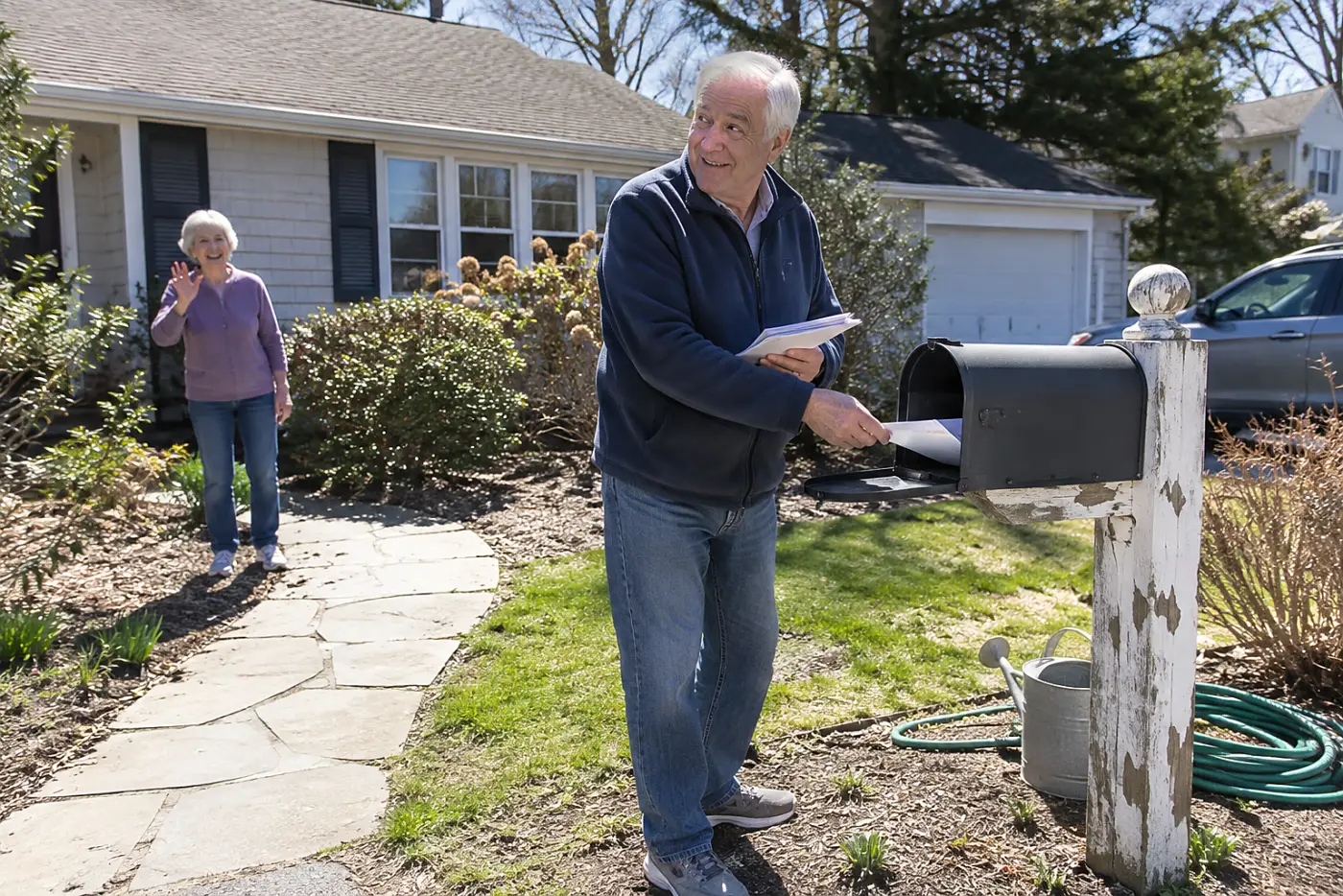A man in his 70s removing envelopes from a mailbox outside his house, with no writing visible.