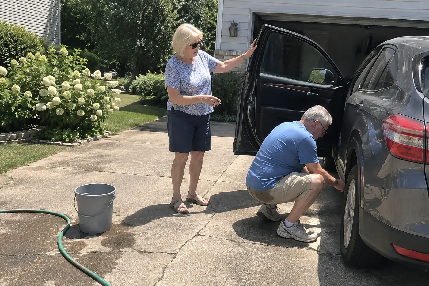Older woman speaking with her husband beside their parked car in the driveway.