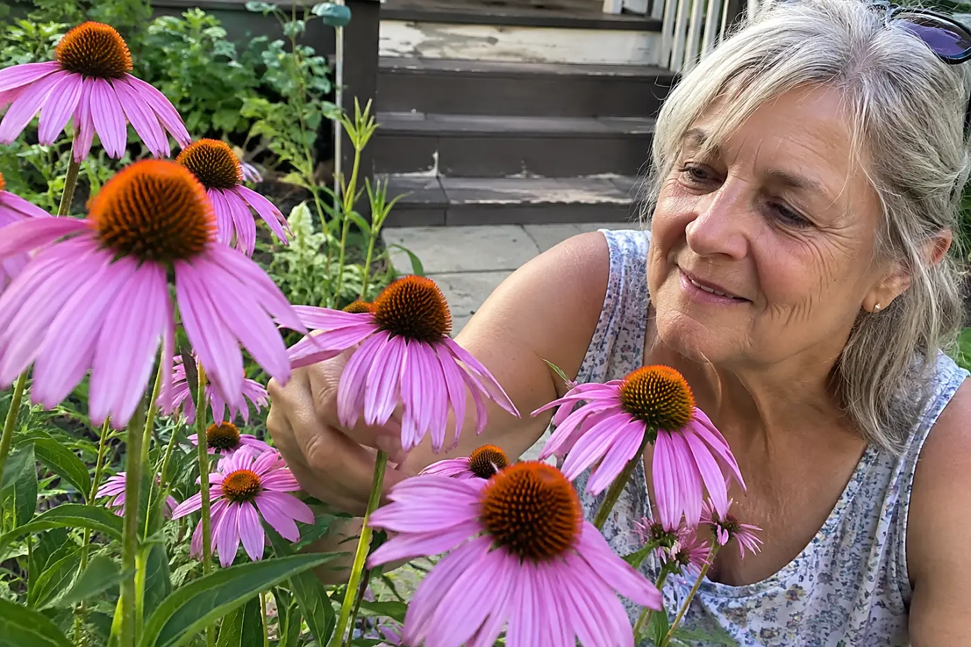 A woman in her sixties gently touches purple coneflowers growing near garden steps.