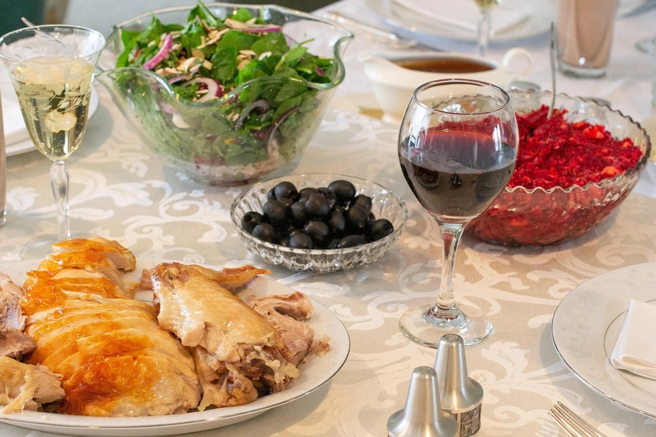 Thanksgiving dinner table with sliced turkey, spinach salad, cranberry relish, black olives, gravy and wine glasses on a damask tablecloth