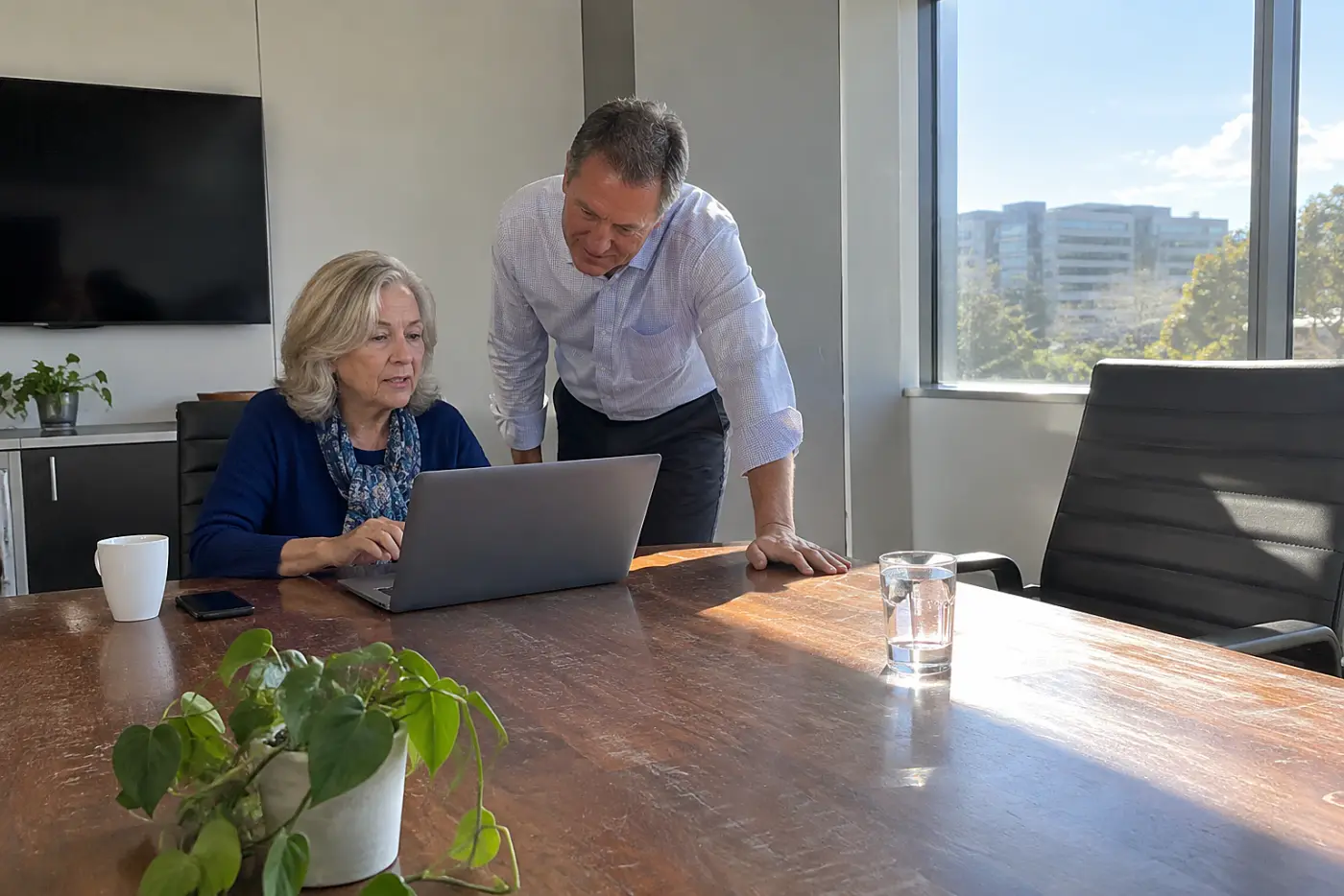 Older woman opening a file on her laptop during a conference room meeting.