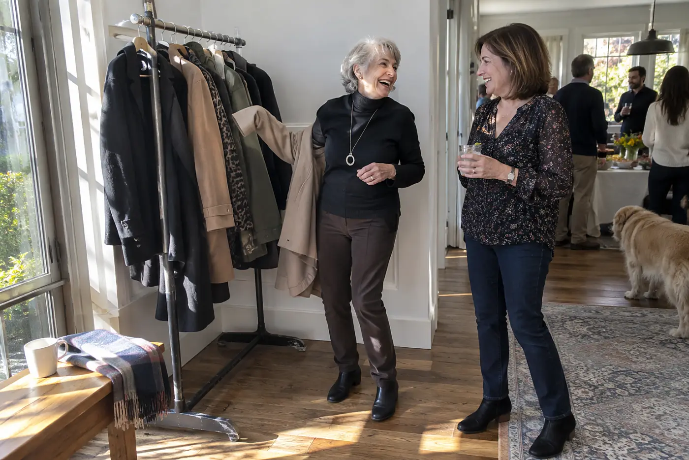 Older woman speaking with a friend beside a rack of coats at a party.