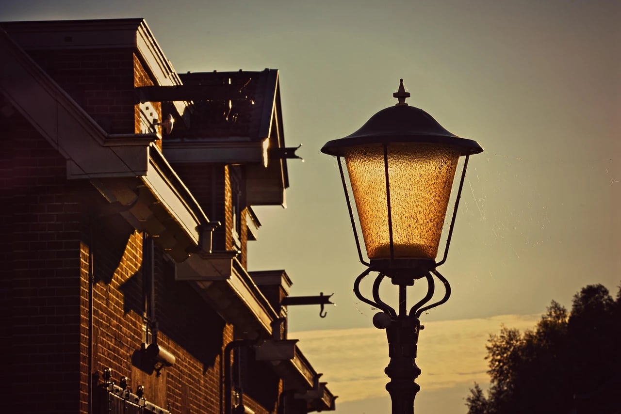 Vintage iron streetlight with a glowing amber lantern at dusk beside a brick building