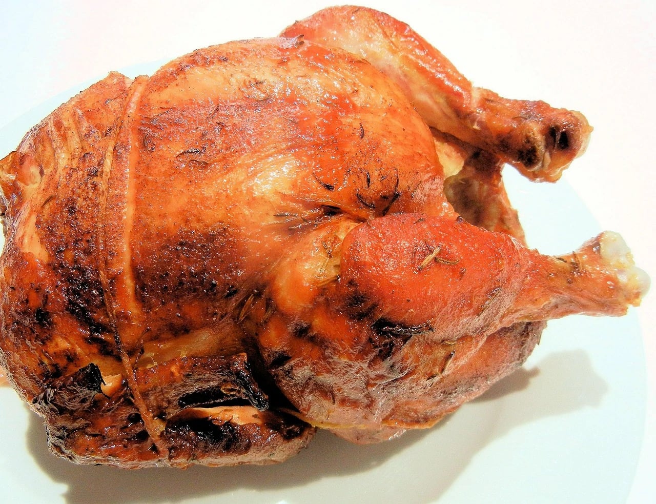 Whole golden-brown rotisserie chicken with herbs and twine on a white plate, close-up view