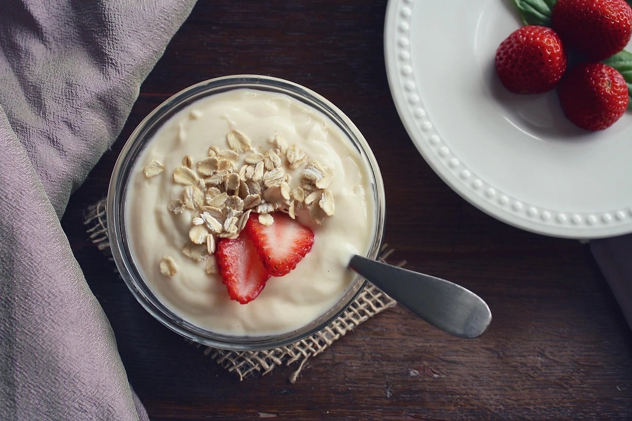 Overhead view of a glass bowl of creamy plain yogurt topped with oats and strawberry slices