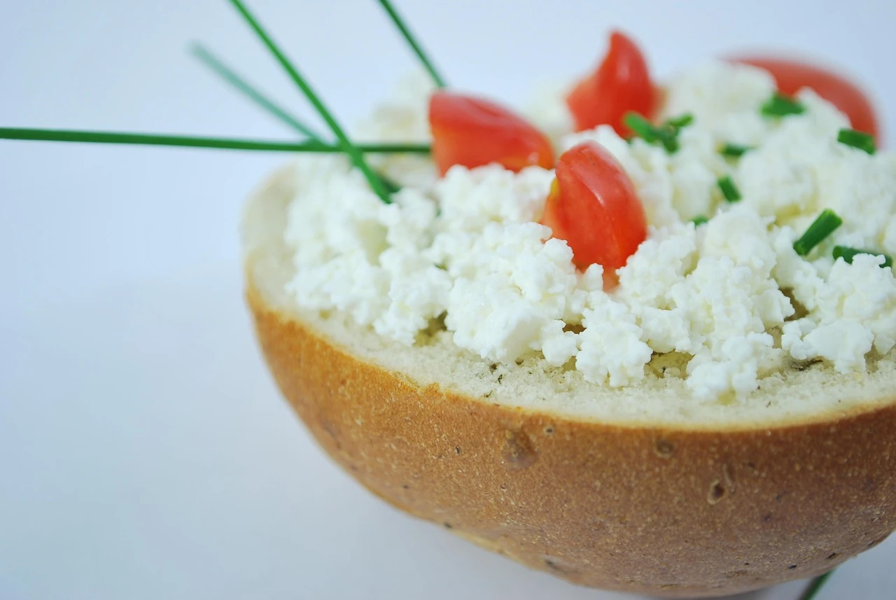 Bread roll half spread with cottage cheese, topped with fresh tomato pieces and chopped chives