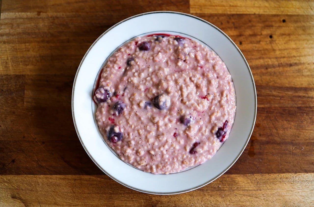 Overhead view of a white bowl of creamy pink oatmeal with blueberries on a wooden table