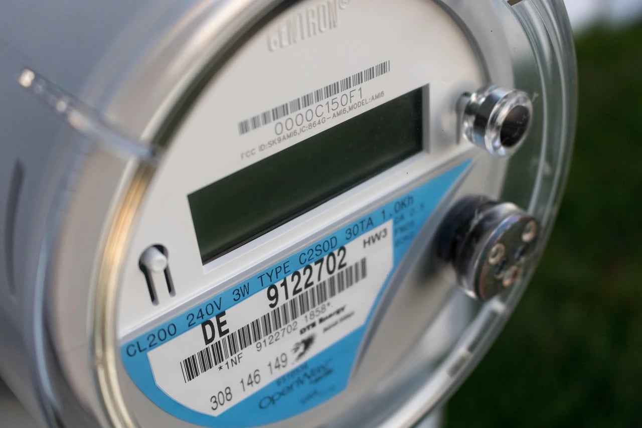 Close-up of a digital electric utility meter with blue label and barcodes mounted outdoors
