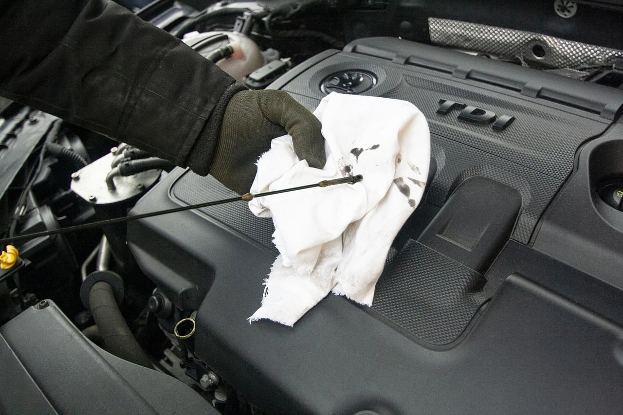 Gloved hand wiping an oil dipstick with a white rag over a car engine