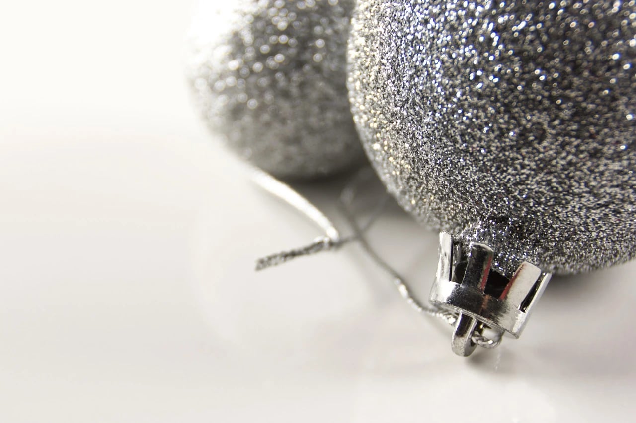 Two silver glitter ball ornaments with metal caps and thin cords resting on a white surface