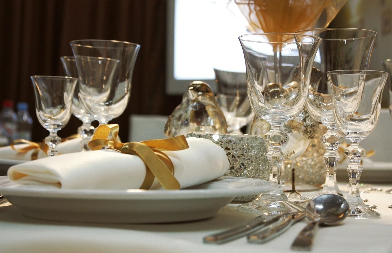 White table setting with napkin tied in gold ribbon, crystal glasses and gold decorative accents
