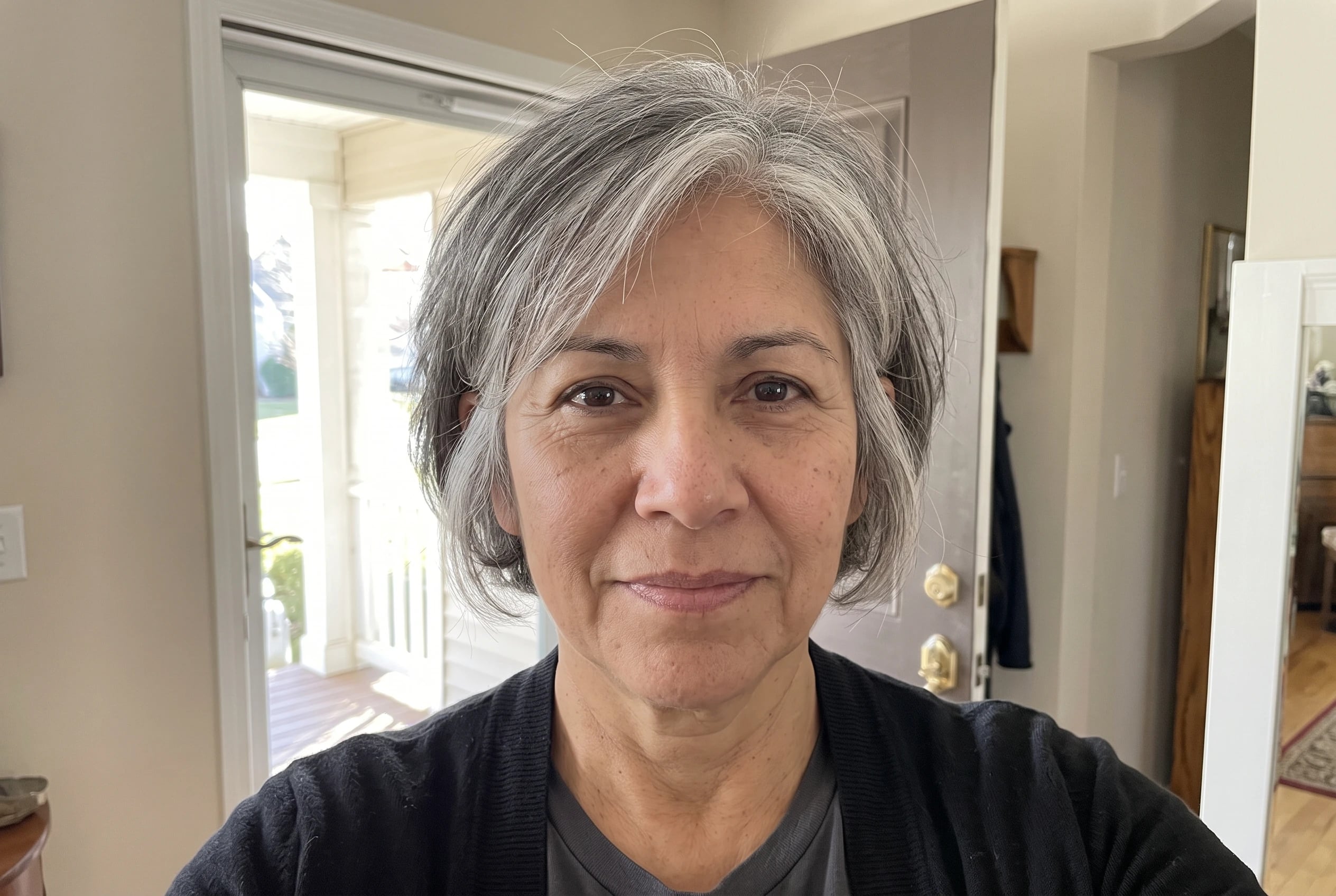An ear-length bob with soft layers cups the jaw of a woman in her fifties standing in a sunlit entryway.