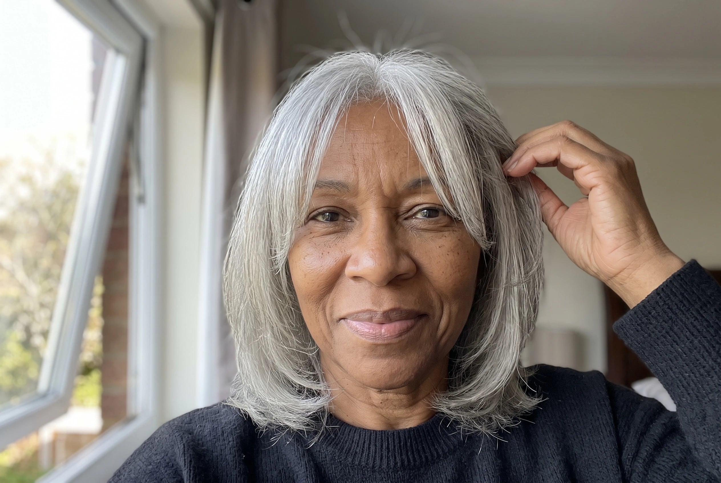 A layered cut with curtain bangs frames a woman in her seventies beside an open bedroom window.