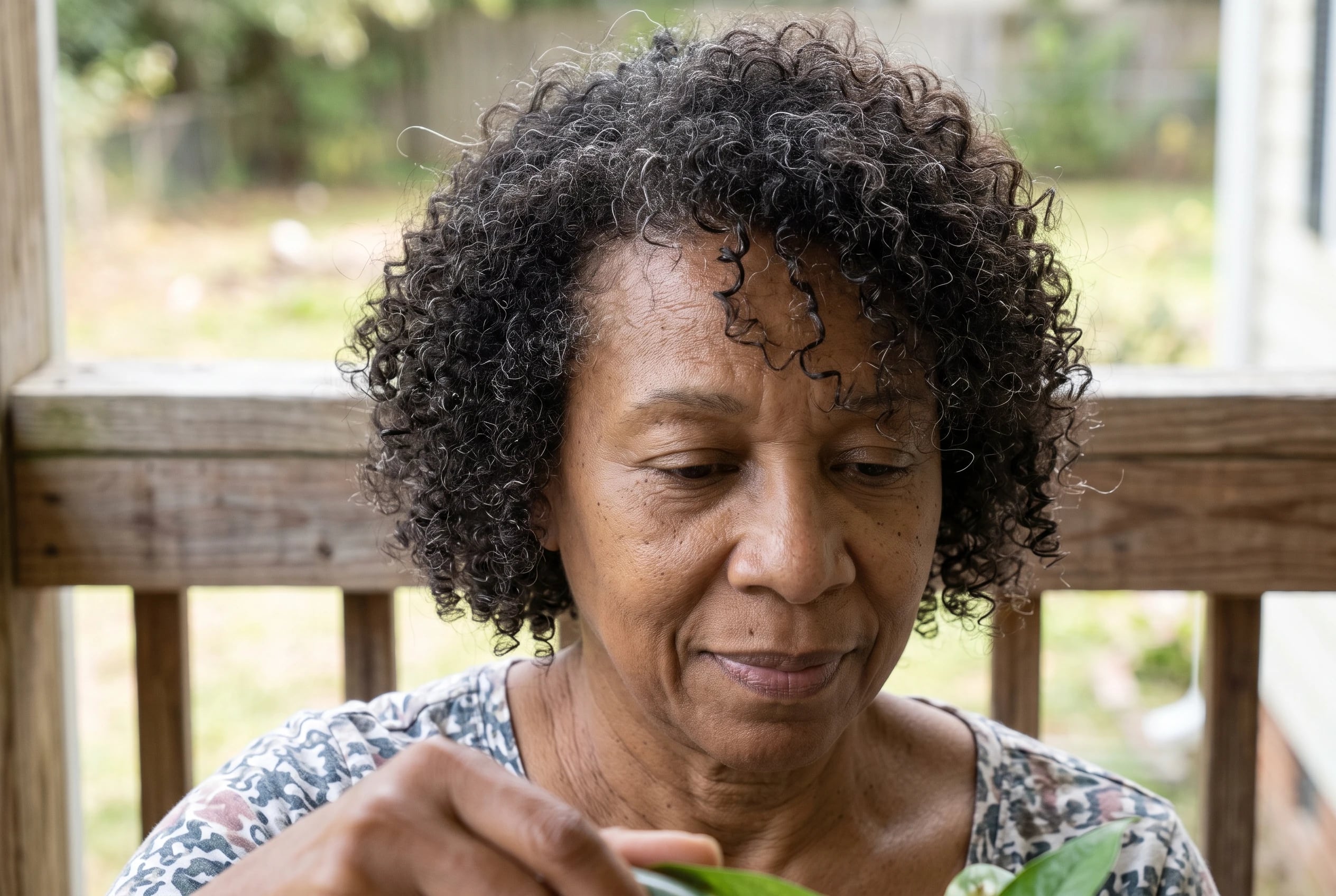A curly bob with rounded layers frames a woman in her sixties as she waters plants on her porch.