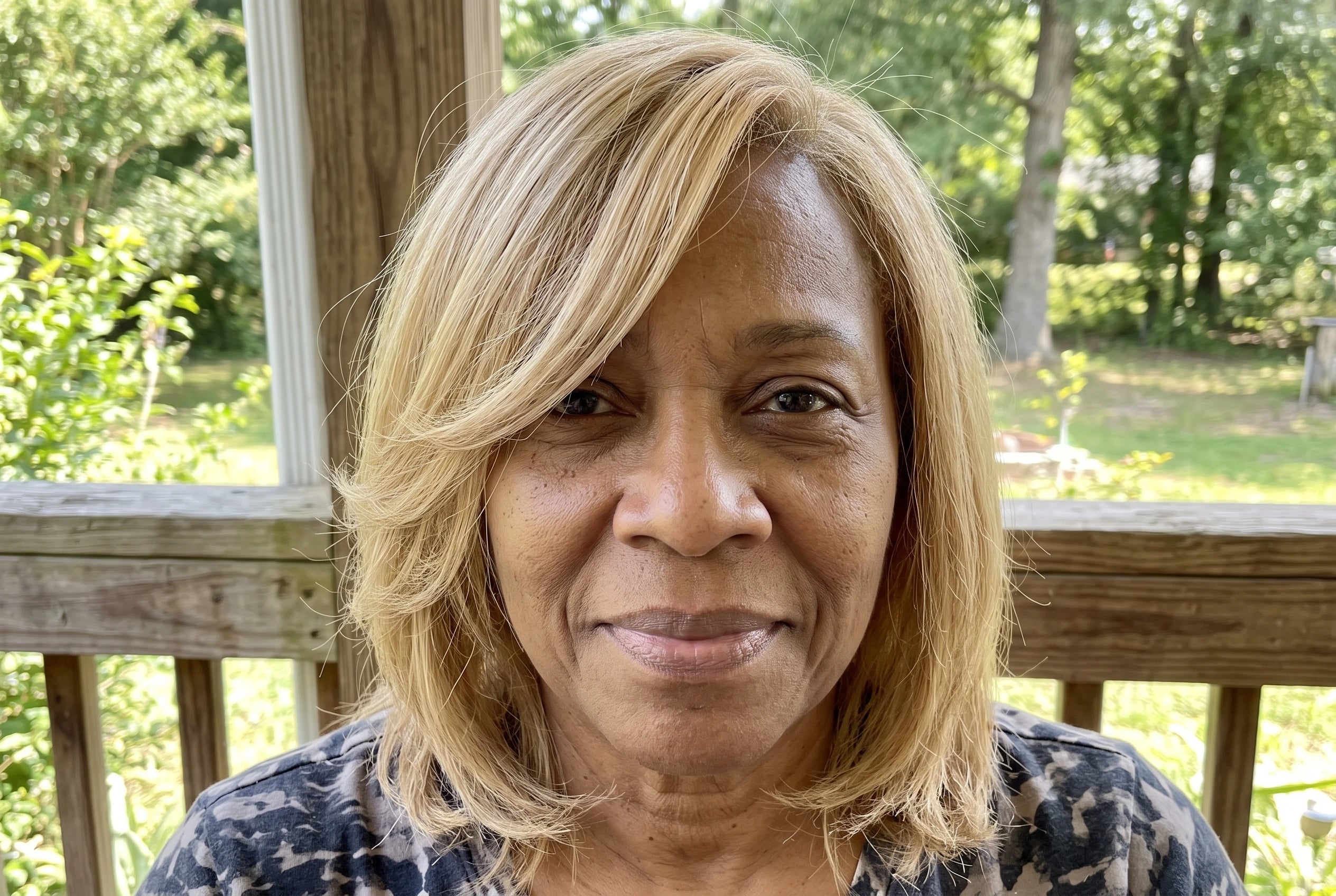 A shoulder-grazing cut with a swoop crosses the cheek of a woman in her sixties standing on her porch.