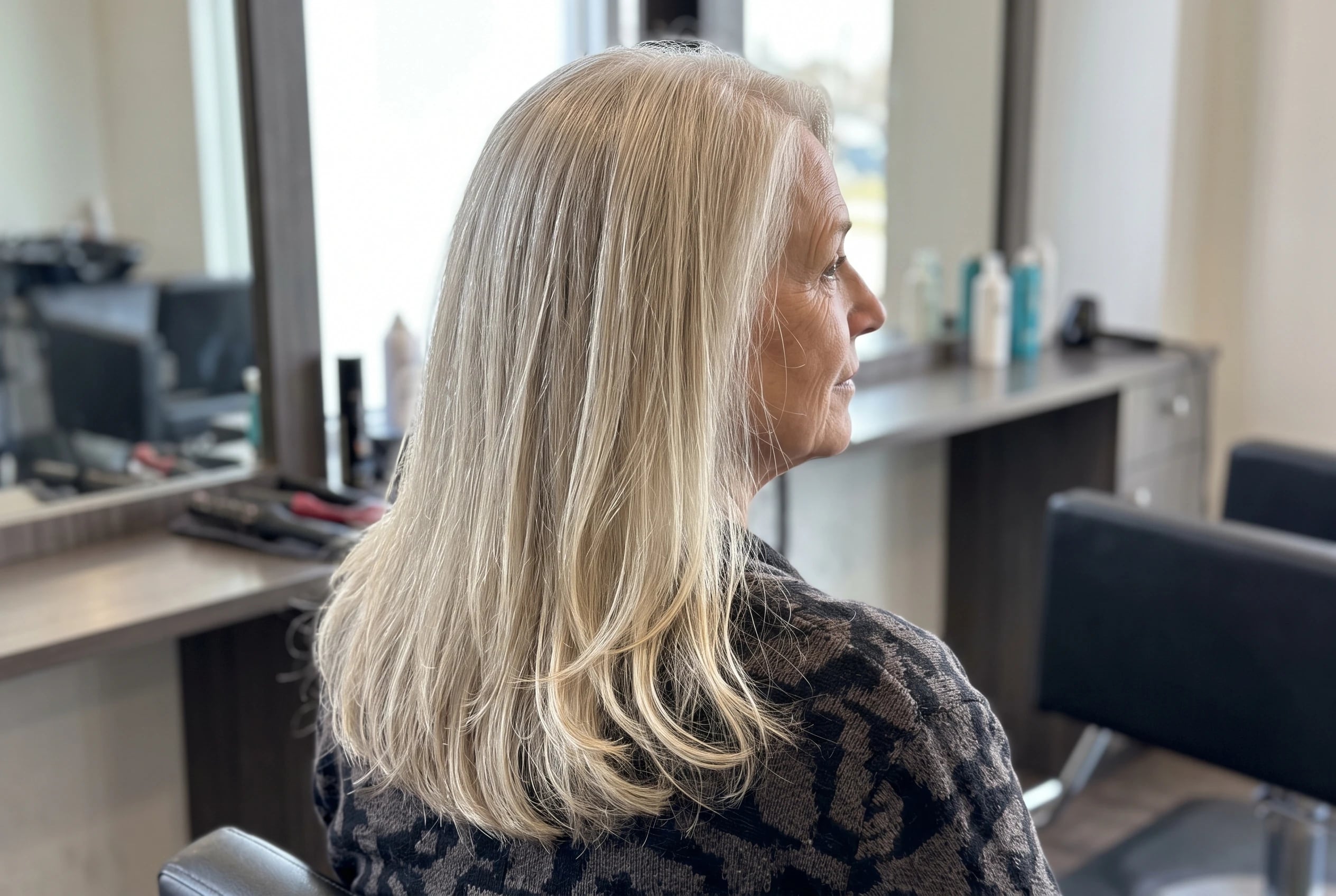 Long hair with invisible layers keeps its full outline as a woman over 50 turns away from a mirror in a salon.