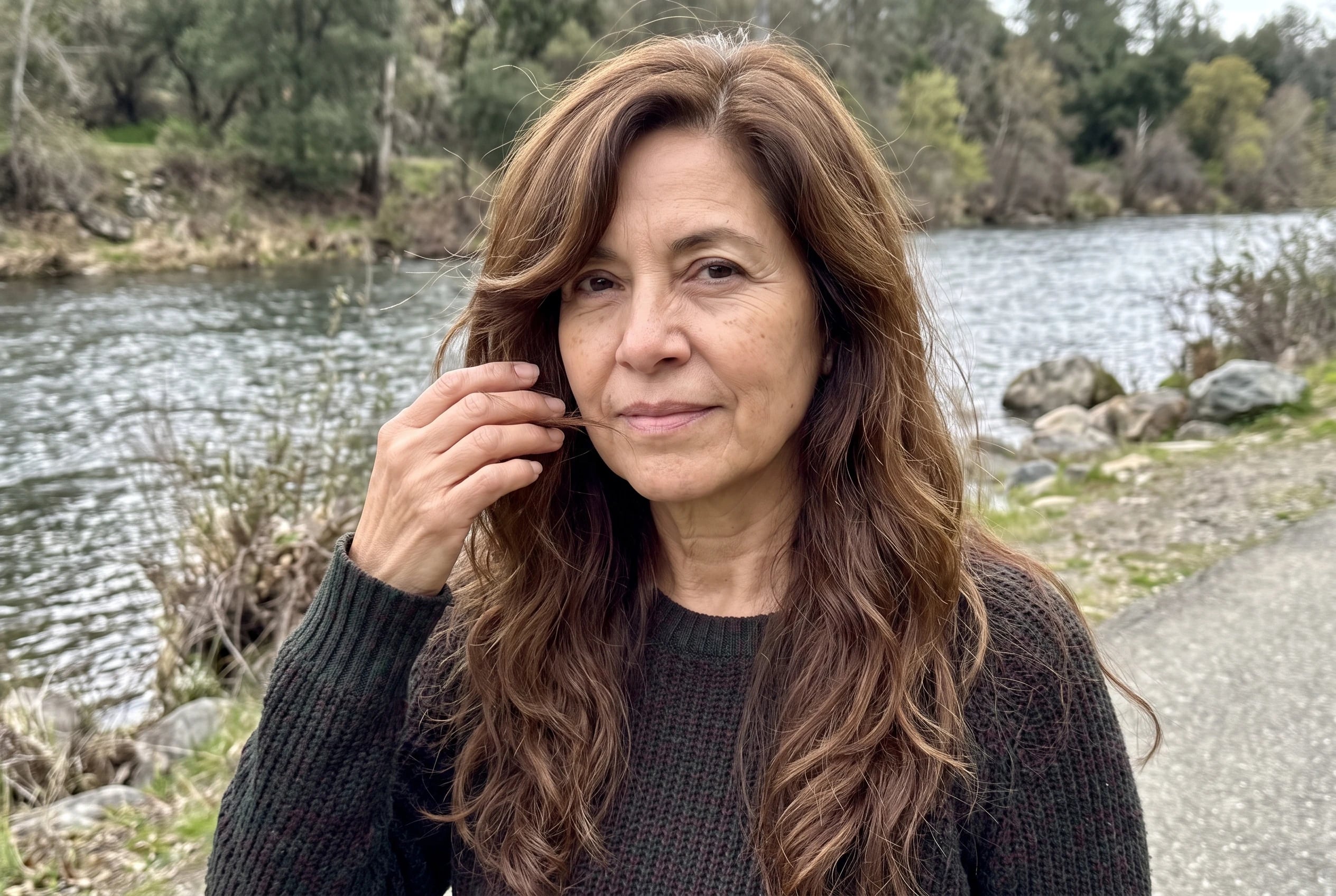 A deep side part with waves sweeps across the forehead of a woman over 50 walking beside a river.