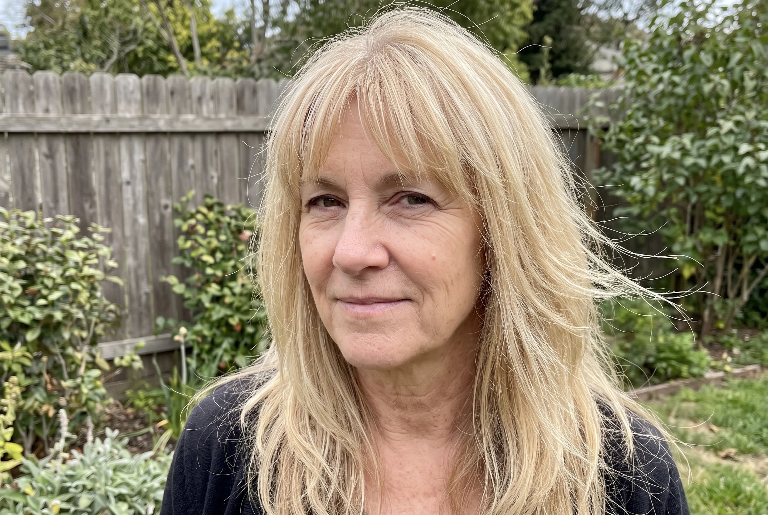 A long shag with wispy bangs moves around the face of a woman over 50 stepping out into her garden.