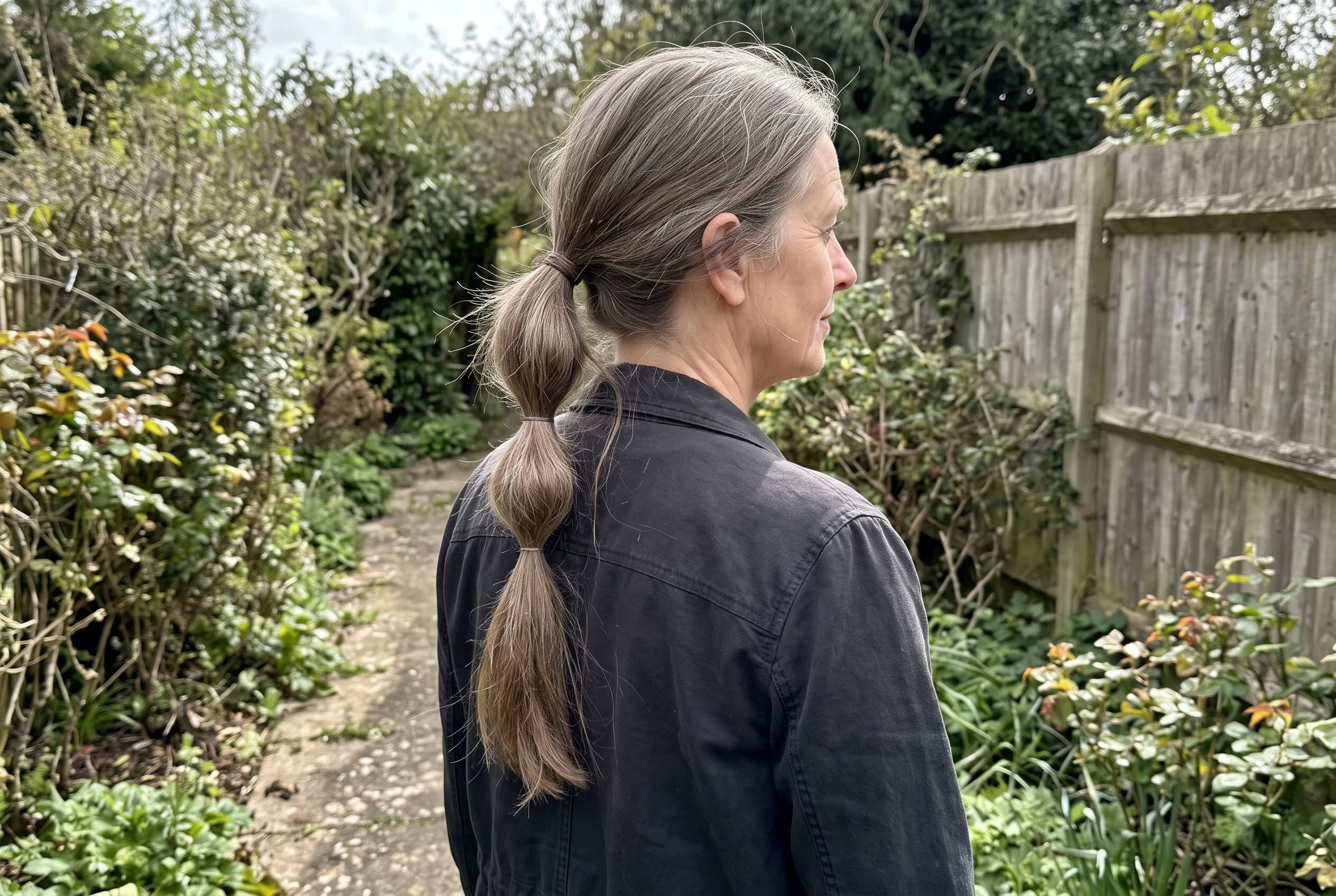 A low bubble ponytail runs down the back of a woman in her late fifties as she walks through a market aisle.