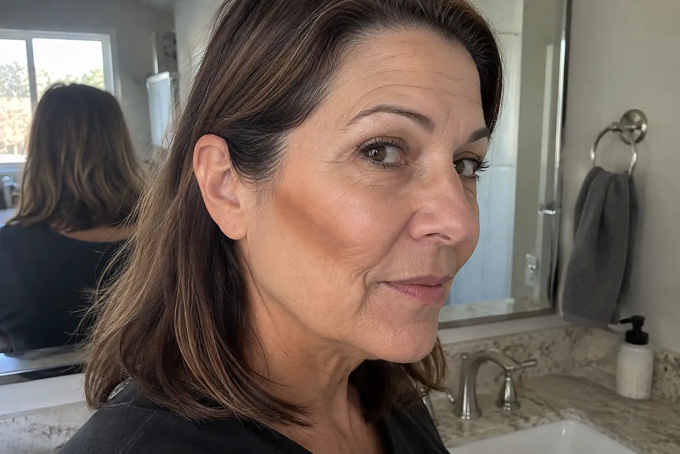 A woman in her fifties wears a blunt stripe of contour makeup along her cheekbone.